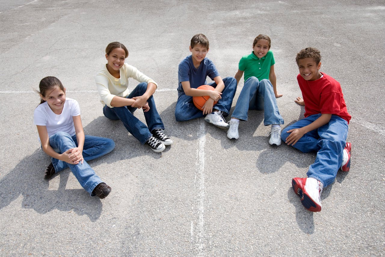Accueil A diverse group of teenagers sitting on concrete, enjoying friendship and sports outdoors.