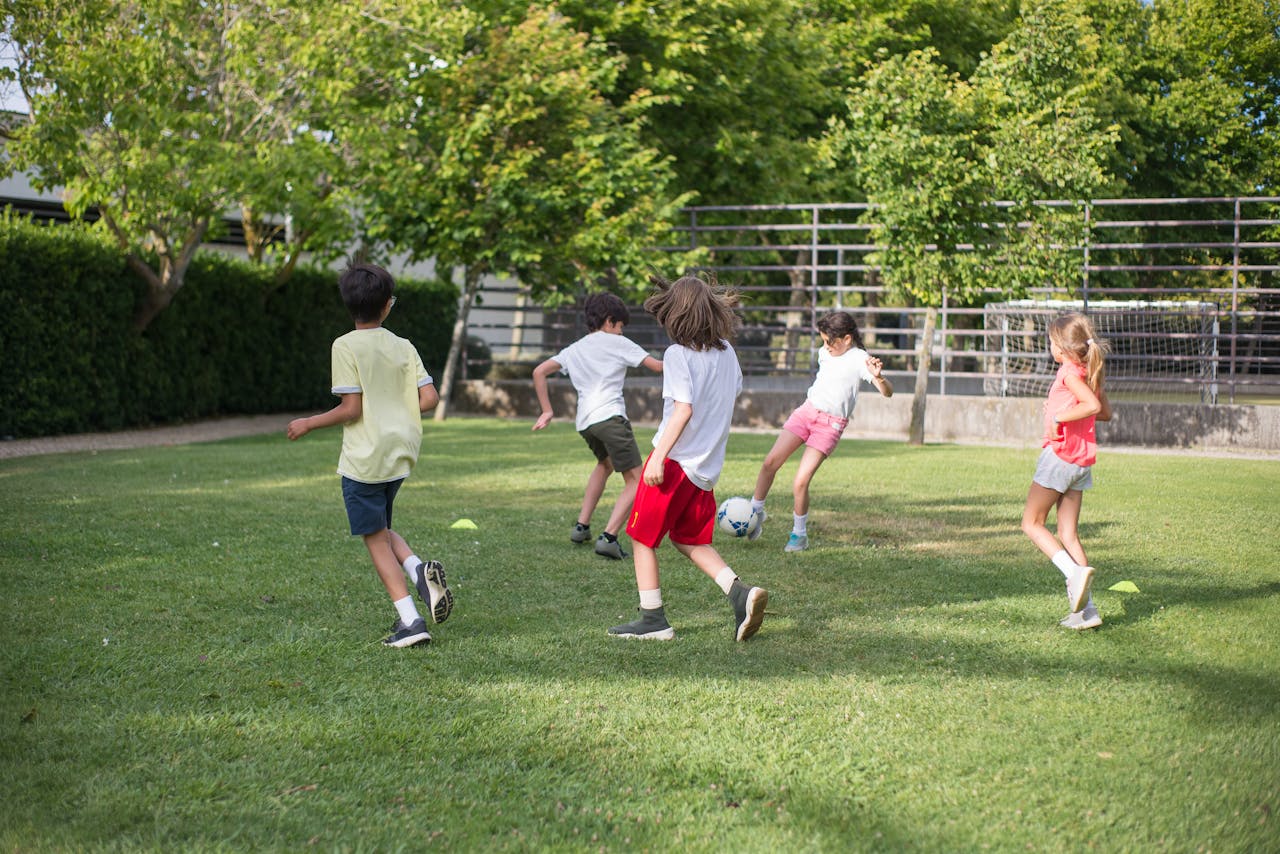 Accueil Group of kids having fun playing soccer on a grassy field on a sunny day.